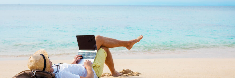 Man,Working,On,Laptop,Computer,While,Relaxing,On,The,Beach