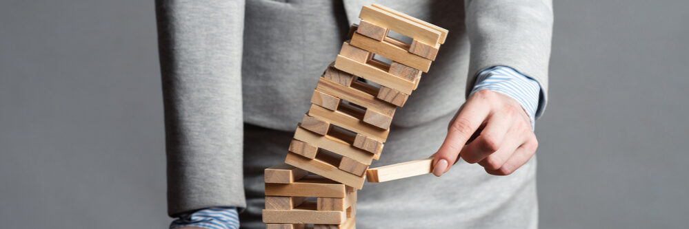 Businesswoman,Removing,Wooden,Block,From,Falling,Tower,On,Table.,Management